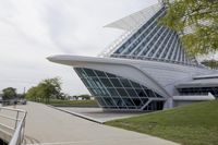 people riding on a skateboard past a building with a curved roof that has large windows