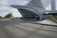 people riding on a skateboard past a building with a curved roof that has large windows