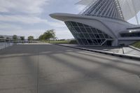 people riding on a skateboard past a building with a curved roof that has large windows