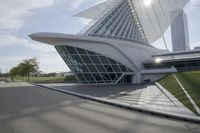 people riding on a skateboard past a building with a curved roof that has large windows