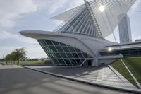 people riding on a skateboard past a building with a curved roof that has large windows