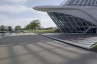 people riding on a skateboard past a building with a curved roof that has large windows