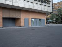 a person on their skateboard is passing by a building with closed doors and a glass door
