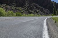 a mountain slope is in the background while a skateboarder rides along the road