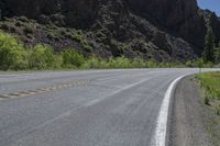 a mountain slope is in the background while a skateboarder rides along the road