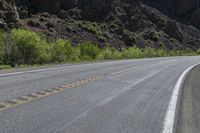 a mountain slope is in the background while a skateboarder rides along the road