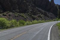 a mountain slope is in the background while a skateboarder rides along the road