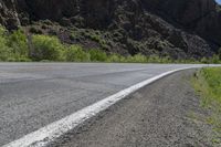 a mountain slope is in the background while a skateboarder rides along the road