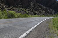 a mountain slope is in the background while a skateboarder rides along the road