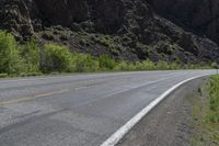 a mountain slope is in the background while a skateboarder rides along the road