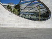 a young man rides his skateboard near an arch in the background that is reflecting the sky and palm trees