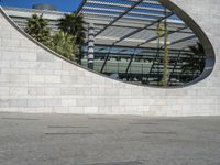 a young man rides his skateboard near an arch in the background that is reflecting the sky and palm trees