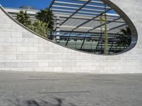 a young man rides his skateboard near an arch in the background that is reflecting the sky and palm trees