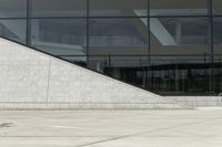 the boy is skateboarding down the sidewalk near a building with a glass window behind him