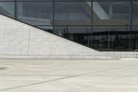 the boy is skateboarding down the sidewalk near a building with a glass window behind him