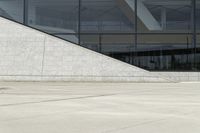 the boy is skateboarding down the sidewalk near a building with a glass window behind him