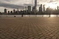 the young boy is riding his skateboard near a river bank and tall buildings in the background