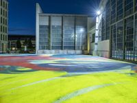 a skateboarder rides down a colorful painted floor in an outdoor building at night