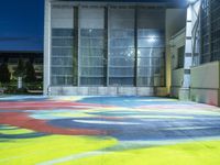 a skateboarder rides down a colorful painted floor in an outdoor building at night