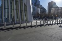 a skateboarder riding down the side of an empty city street, surrounded by glass and concrete buildings