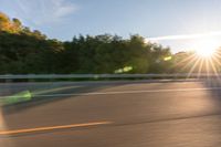 a man riding on a skateboard down a road near trees and the sun rising