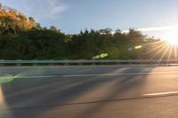 a man riding on a skateboard down a road near trees and the sun rising