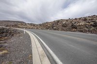 a man riding a skateboard down a paved road surrounded by rocky mountains and boulders