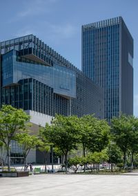 a man riding a skateboard across a plaza next to tall buildings with trees in front of it