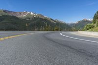 a person riding a skateboard on a road by a mountainous setting with mountains in the background