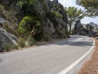 a person riding their skateboard down a winding road surrounded by cliffs and trees at the side of a hill