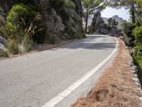 a person riding their skateboard down a winding road surrounded by cliffs and trees at the side of a hill