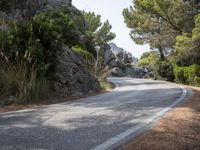 a person riding their skateboard down a winding road surrounded by cliffs and trees at the side of a hill