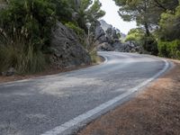 a person riding their skateboard down a winding road surrounded by cliffs and trees at the side of a hill