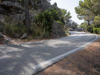 a person riding their skateboard down a winding road surrounded by cliffs and trees at the side of a hill