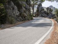 a person riding their skateboard down a winding road surrounded by cliffs and trees at the side of a hill