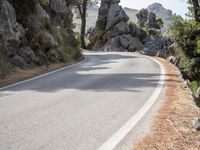 a person riding their skateboard down a winding road surrounded by cliffs and trees at the side of a hill