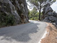 a person riding their skateboard down a winding road surrounded by cliffs and trees at the side of a hill