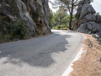 a person riding their skateboard down a winding road surrounded by cliffs and trees at the side of a hill