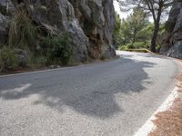 a person riding their skateboard down a winding road surrounded by cliffs and trees at the side of a hill