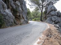 a person riding their skateboard down a winding road surrounded by cliffs and trees at the side of a hill