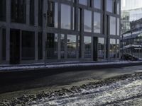 the person is riding a skateboard down the street in the snow near a building