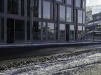 the person is riding a skateboard down the street in the snow near a building