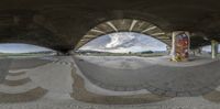 a skateboarder is seen riding on the pavement through an overpass while another skateboard sits in a distance