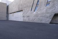 a man on a skateboard on the street by a large concrete building in the background