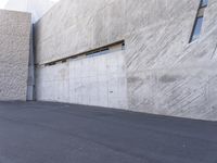 a man on a skateboard on the street by a large concrete building in the background