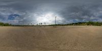 a man is on his skate board on a dirt court while cloudy skies can be seen over the landscape