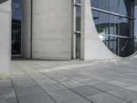 a person skateboarding and doing a trick on the sidewalk outside a building with large windows