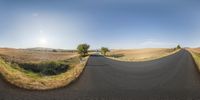 a man on a skateboard riding down a dirt road in a countryside under a blue sky