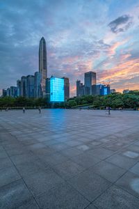 people are riding skateboards around in a park near the city skyline with high rise buildings at twilight