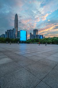 people are riding skateboards around in a park near the city skyline with high rise buildings at twilight